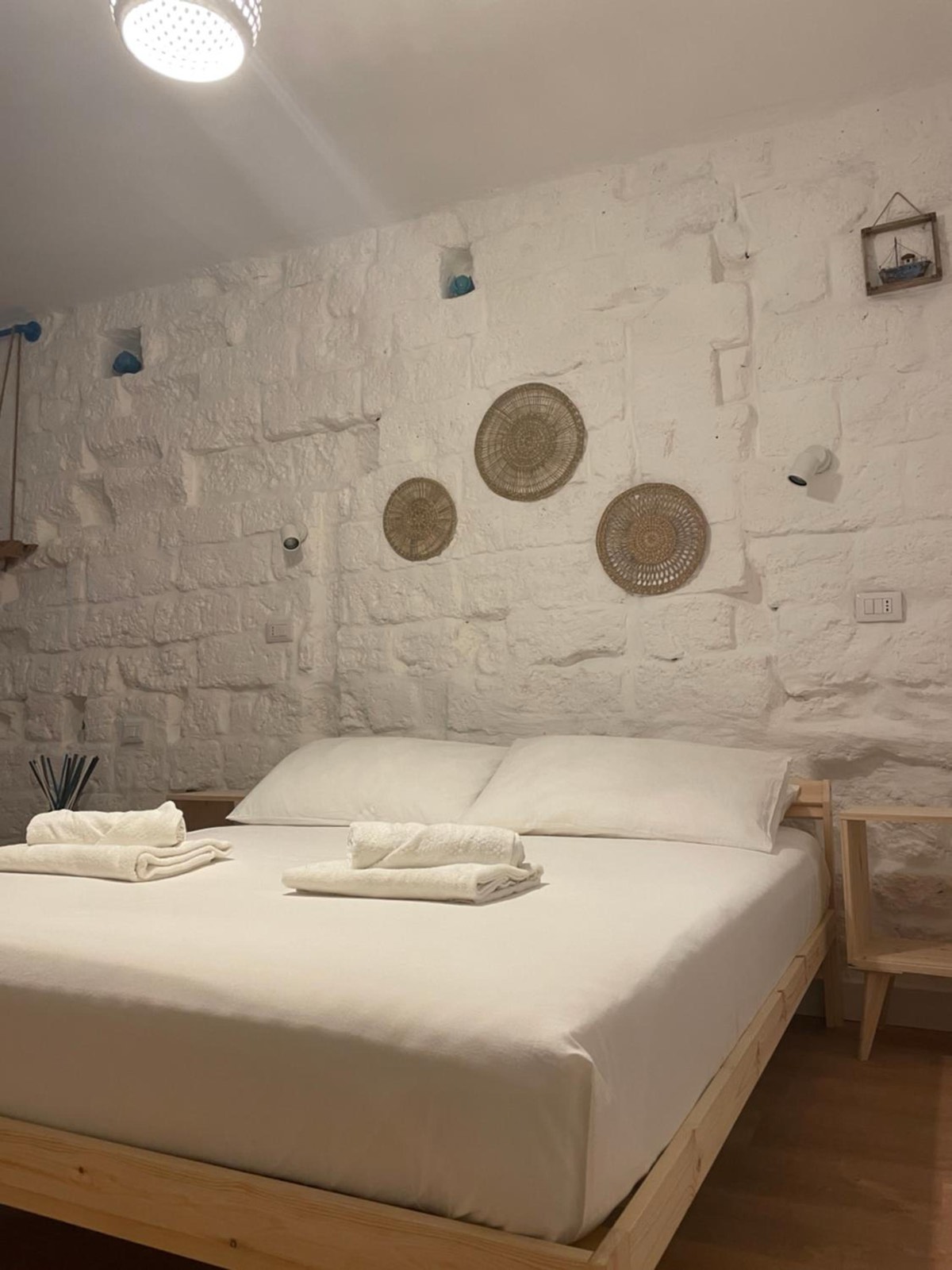 Un letto matrimoniale e tre piatti di paglia appesi al muro in pietra