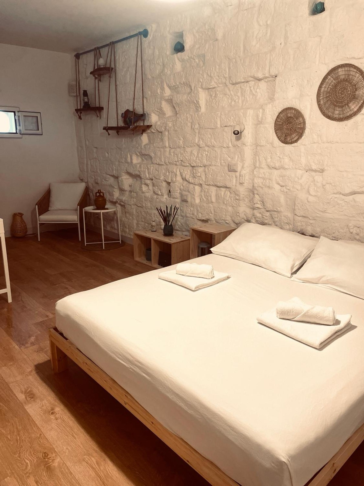 Il letto matrimoniale, una poltroncina e il muro in pietra con i piatti di paglia