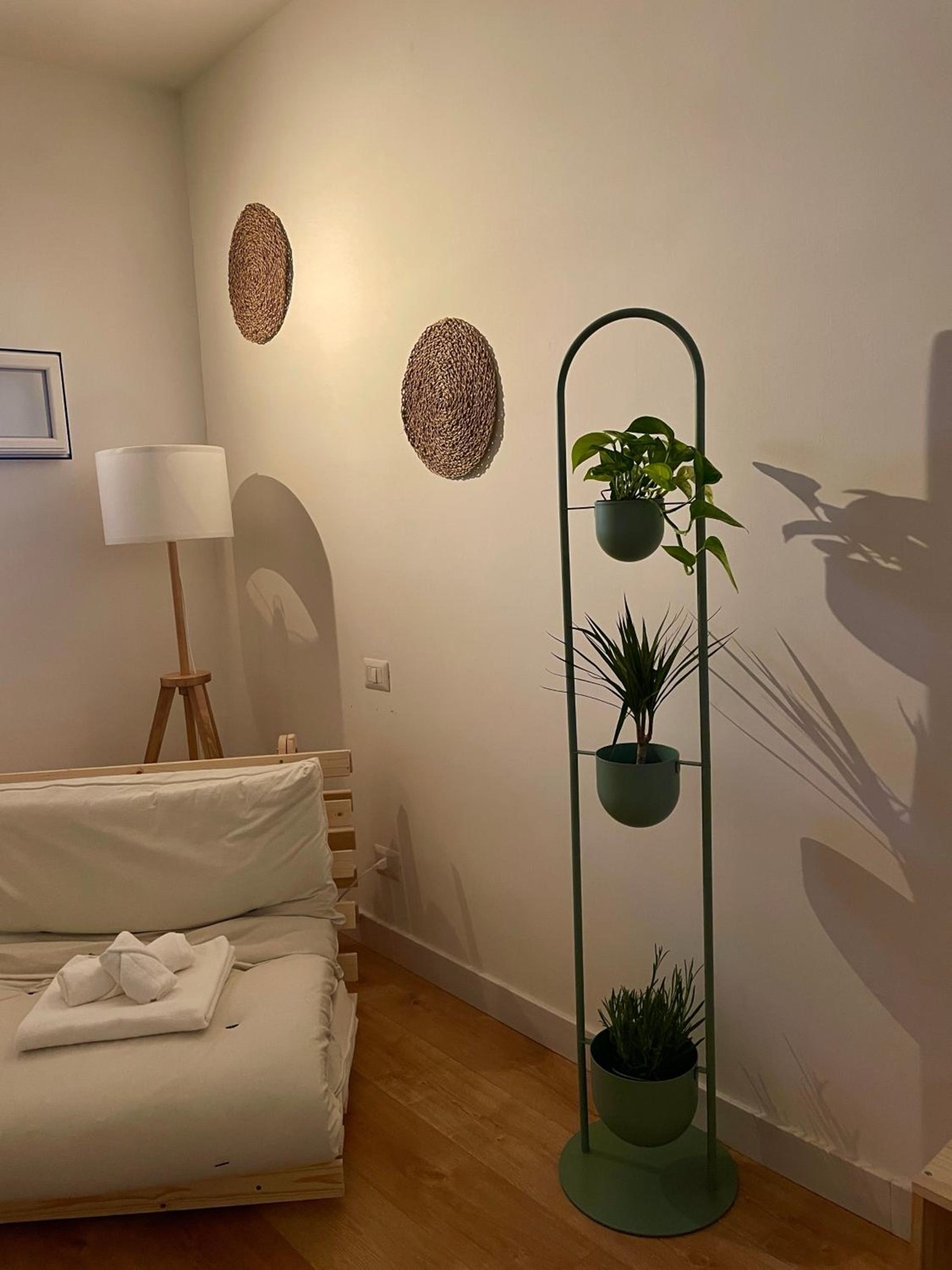 Un letto, una lampada a stelo e un’alzata di metallo con le piante
